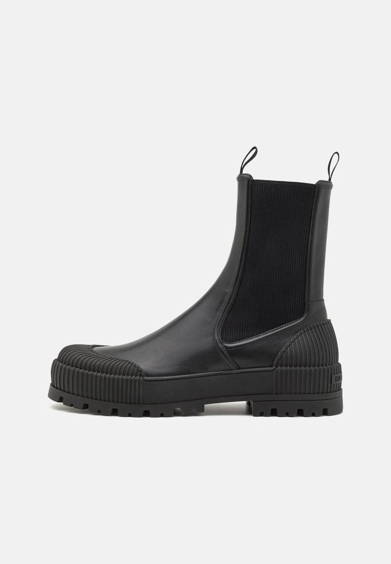 Bottine en cuir noir avec bout et talon en caoutchouc nervuré, panneaux latéraux élastiques, languettes de traction et semelle épaisse à crampons.