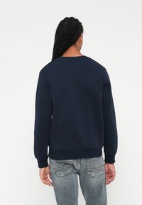 Mørkeblå genser med rund hals og ribbestrikket mansjetter. Laget av mykt stoff, med et enkelt, rent design uten synlige grafikker.