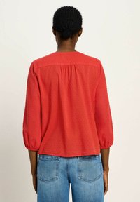 Rote Bluse mit Puffärmeln aus strukturiertem Stoff mit kleinen erhabenen Punkten, mit rundem Ausschnitt und lockerer Passform am Rücken.