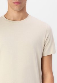 Beidzis īso piedurkņu krekls, kas izgatavots no kokvilnas; ar apaļu kakla izgriezumu un gludu, vienmērīgu tekstūru ar smalku stiepšanos.