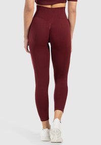 Leggings taille haute en bordeaux, en matériau extensible, design ajusté, texture lisse, accompagnés de chaussures de sport blanches.