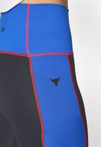 Leggings sportivi a vita alta con pannelli blu e neri e cuciture rosse. Include un dettaglio con logo di un toro nero sulla coscia.