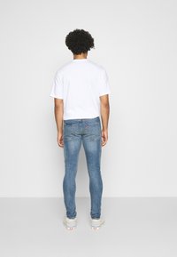Vaqueros ajustados de color azul con textura desgastada, con bolsillos traseros y detalles de costura sutiles, acompañados de una camiseta de algodón blanca lisa.