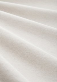 Világos bézs szövet, sima, puha textúrával, redőkbe hajtva, finom szőtt mintával és egységes színnel az egész felületen.