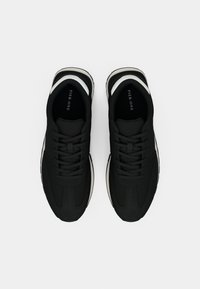 Μαύρα αθλητικά παπούτσια με άνω μέρος από λείο ύφασμα, κορδόνια, λευκές λεπτομέρειες στη σόλα και σχεδιασμό με στρογγυλή μύτη. Περιλαμβάνεται ραφή με έντονη αντίθεση.
