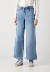 Lyseblå vide jeans laget av denim, med høy midje, fem lommer og subtil slitasje. Kombinert med grå snøring sko.