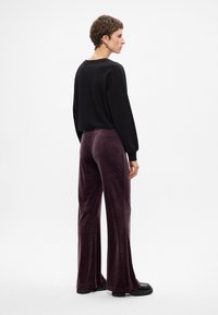 Μαύρη μπλούζα με μακριά μανίκια και μοβ βελούδινες καμπάνες. Το σύνολο διαθέτει χαλαρή εφαρμογή και λεία υφή, συμπληρωμένο με μαύρες λείες κολόνες.