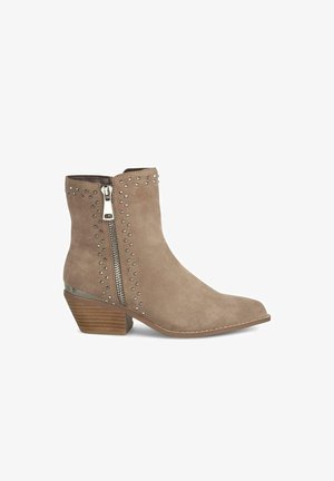Bottine en suedine taupe avec un bout pointu, une fermeture éclair sur le côté et des accents en studs métalliques. Dispose d'un talon en bois empilé pour plus de stabilité.