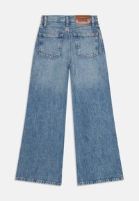 Jeans a gamba larga di colore azzurro chiaro con un effetto sbiadito, dotati di una patta in pelle marrone sulla vita posteriore e due tasche sul retro. Dettaglio con orlo strappato.