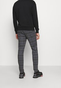 Sudadera negra con puños acanalados, combinada con pantalones de cuadros grises que presentan líneas azules y negras, y zapatillas atléticas negras.