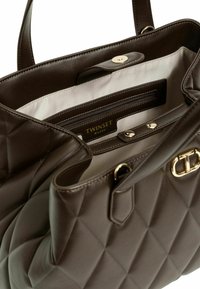 Borsa a tracolla marrone trapuntata con dettagli in metallo dorato, dotata di una tasca interna con zip e una fodera liscia. Etichetta del brand visibile all'interno.
