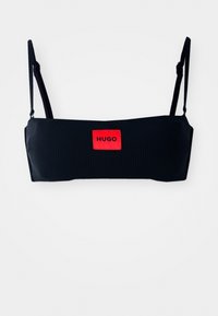 Svart ribbestrikket bandeau-top med justerbare stropper og en fremtredende rød etikett med "HUGO" i svart tekst. Glatt tekstur, minimalistisk design.