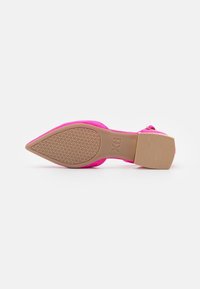 Zapato de tacón alto de ante rosa con punta afilada, suela de goma beige y patrón de agarre texturizado. Acentos de hardware dorado en el tacón.
