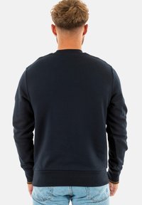 Sudadera azul marino con un cuello y puños acanalados, con una textura suave y un corte clásico, combinada con jeans de un azul claro.