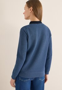Pull-over à rayures bleu marine avec un col contrastant, texture douce, poignets et ourlet côtelés, associé à un jean bleu clair.