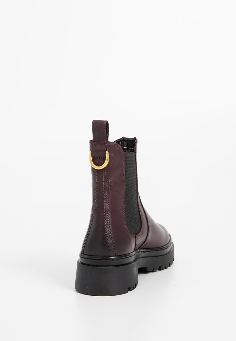 Botas de tobillo de cuero burdeos con una suela gruesa negra, paneles laterales elásticos y un lazo de metal dorado en la parte trasera para facilitar su uso.