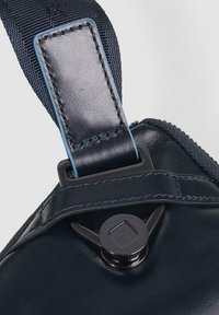 Donkerblauwe leren tasriem met een glanzende afwerking, voorzien van een vierkante zwarte metalen sluiting en blauwe stiknaden langs de randen.