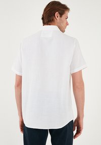 Witte shirt met korte mouwen van linnen, met een kraag, een rechte achterkant en een klein rechthoekig label bij de hals.