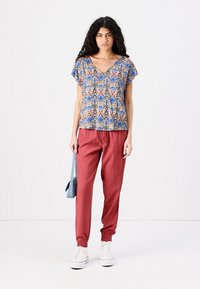 Multicolored patterned short-sleeve top in blue, red, and cream with a V-neck; paired with rust-colored drawstring pants and white sneakers.