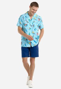 Short-sleeve, light blue shirt with a playful print of colorful characters, paired with navy shorts and white sneakers.