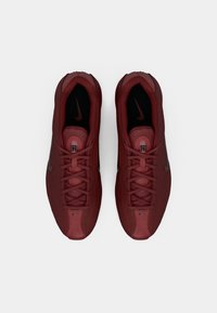 Tumši sarkani Nike sporta apavi ar melniem iekšējiem zolīšiem, redzamām swoosh logo un šņorēm, skatīti no augšas uz baltu fonu.