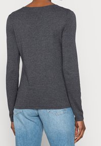 Haut gris à manches longues avec un col rond et une texture côtelée, associé à un jean en denim bleu clair, vu de dos.