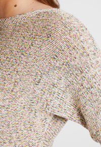 Sweter z dzianiny z wielokolorową, teksturowaną tkaniną, o luźnym kroju i szerokim dekolcie. Widoczne szwy w pastelowych i neutralnych odcieniach.