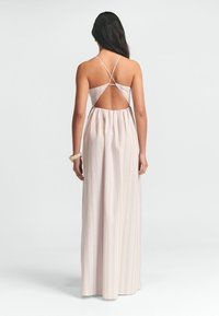 Robe maxi avec une découpe dans le dos, réalisée en tissu léger. Dispose de fines bretelles et de rayures verticales pastel dans des couleurs douces.