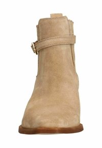 Stivaletto in suede beige con punta arrotondata, cinturino laterale con fibbia e finitura liscia e opaca su un tacco in legno scuro.