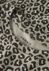 Korte mouwen shirt gemaakt van zachte stof, met een luipaardprint in donkerbruin op een beige achtergrond; bevat een ronde halslijn en een merklabel.