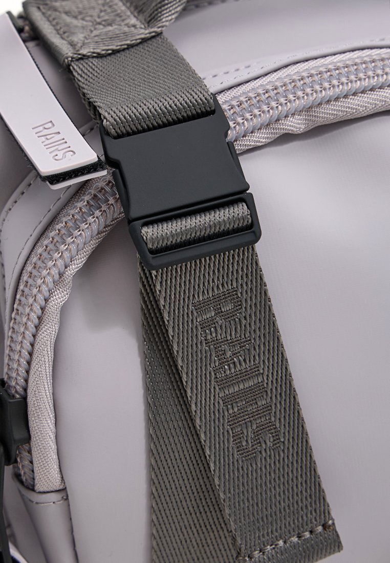 Lichtgrijze rugzak met een gladde, waterbestendige buitenkant. Voorzien van een gestructureerde grijze schouderband, een zwarte plastic sluiting en merkhardware.