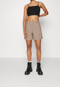 Černý cropped top s dvojitými ramínky, vzorované hnědé šortky s volným střihem a černé šněrovací boty s hrubou podrážkou.