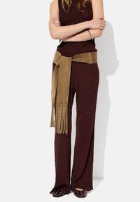 Bordowy, prążkowany sweter oraz szerokie spodnie z tanowym, zamszowym paskiem z frędzlami. Buty na szpilkach z srebrnymi ćwiekami.