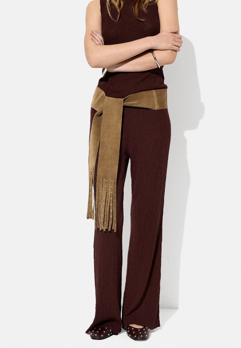 Bordowy, prążkowany sweter oraz szerokie spodnie z tanowym, zamszowym paskiem z frędzlami. Buty na szpilkach z srebrnymi ćwiekami.