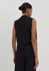 Haut sans manches noir avec un col montant et une coupe décontractée. Fabriqué en tissu texturé, il présente un ourlet légèrement incurvé.