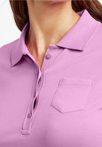 Lavendelpolotröja med krage, två knappar och en liten bröstficka. Slät textur och avslappnad design.