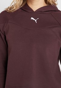 Bordeauxrotem Hoodie mit einer Kängurutasche, strukturierten Schulterpaneelen und einem weißen Puma-Logo auf der Brust. Weicher, strapazierfähiger Stoff.