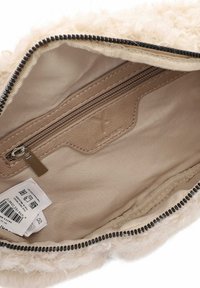 Interno della borsa beige fuzzy con una tasca a zip liscia color tan, fodera morbida e una zip nera a contrasto lungo il bordo.