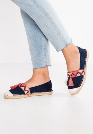 Dunkelblaue Espadrilles mit einer geflochtenen Jutesohle, versehen mit lebhaft gemustertem roten und weißen Stoff sowie dekorativen Quasten am Riemen.