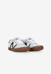 Weiße und graue Sneakers mit schwarzen Akzenten, ausgestattet mit einer Gummisohle und Schnürverschluss. Velours- und Mesh-Materialien mit einem schlichten, geometrischen Design.
