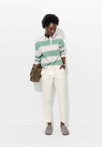 Polo à manches longues rayé vert et blanc, pantalon couleur crème, chaussons à pois et sac à main marron en tissu texturé.