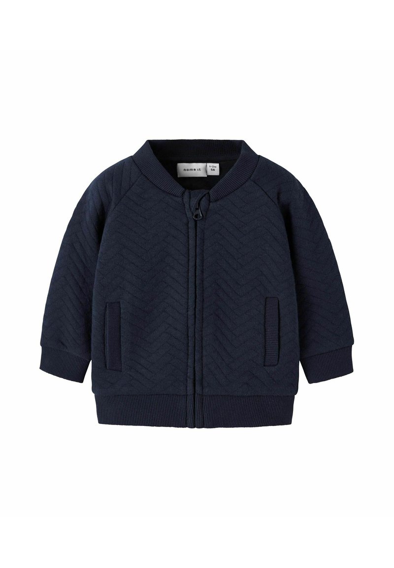 Námorně modrá zipová bunda s herringbone texturou, žebrovanými manžetami a lemem, dvěma předními kapsami, kulatým výstřihem a visačkou uvnitř.