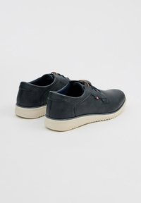 Zapatos azul marino con textura suave, punta redonda, diseño minimalista, suela clara contrastante y pequeño detalle de logo en el costado.