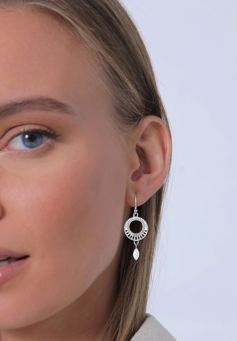 Silberne hängende Ohrringe mit einem kreisförmigen Design und einem offenen Zentrum, strukturierten Details und einem blattförmigen Akzent darunter.