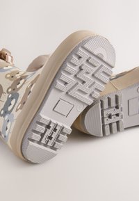 Bottes en caoutchouc avec une base beige, ornées d'un motif ludique d'ours en bleu, marron et crème. Les semelles texturées offrent adhérence et stabilité.