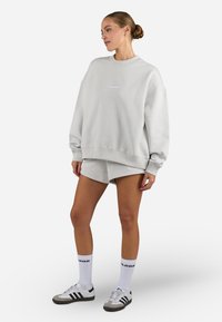 Light grey oversized sweatshirt with crew neck, and matching shorts. Features soft texture, ribbed cuffs, and subtle branding. Paired with white and black sneakers and socks.