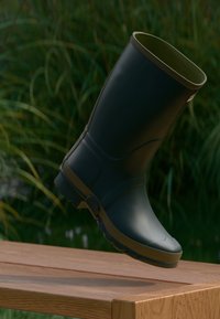 Μαύρη καουτσούκ μπότες με ματ φινίρισμα, στρογγυλή μύτη και υφασμάτινη σόλα. Διαθέτει πράσινο εσωτερικό και χαμηλό τακούνι.