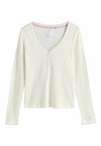 Haut en maille côtelée crème à manches longues avec col en V, trois petits boutons, et bordure festonnée rose sur le col et les poignets.