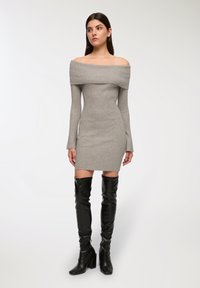 Abito grigio a maglia con spalle scoperte, maniche lunghe e una vestibilità aderente, abbinato a stivali neri in pelle al ginocchio con tacchi chunky.