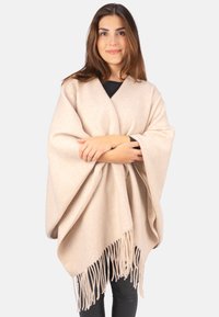 Beiger Poncho mit Fransen am Saum, gefertigt aus samtigem, wollartigem Material. Lockere Passform, die sich angenehm über die Schultern legt.